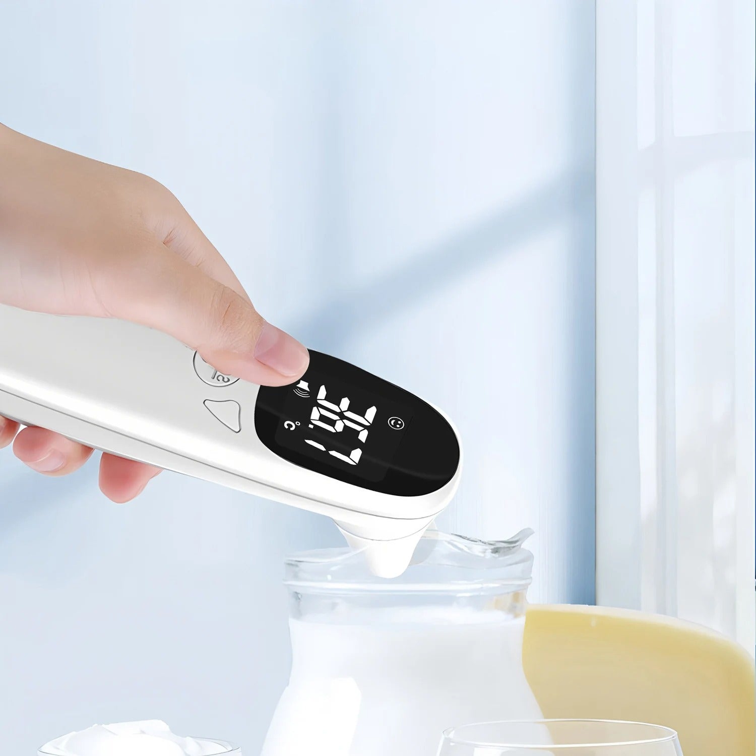 Hand holding a white electronic device with digital display over a glass container on a light blue background.