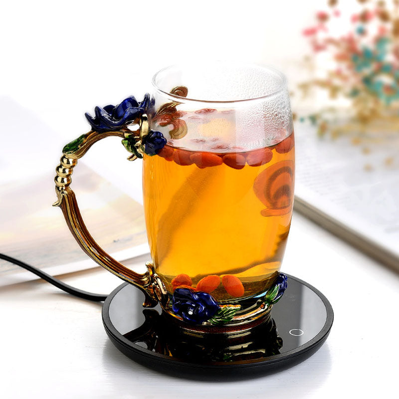 Glass mug with floral handle filled with tea on a black coaster