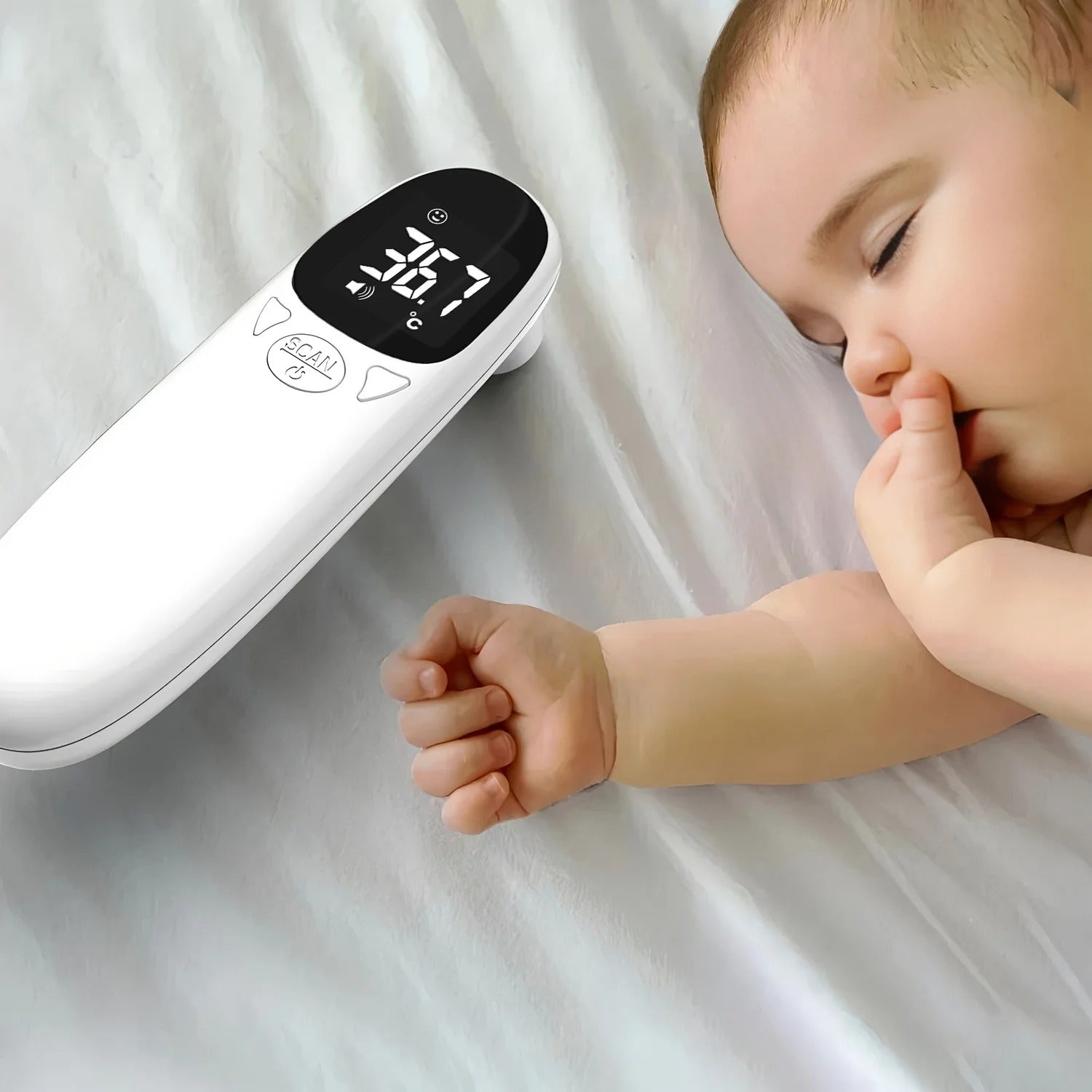 Baby lying on a white surface next to a digital thermometer displaying a temperature.