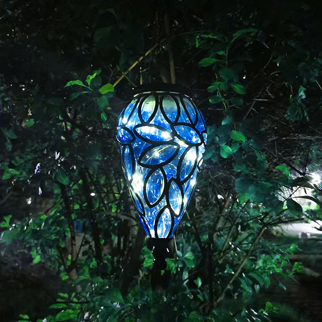 Decorative blue solar light hanging among green foliage at night.
