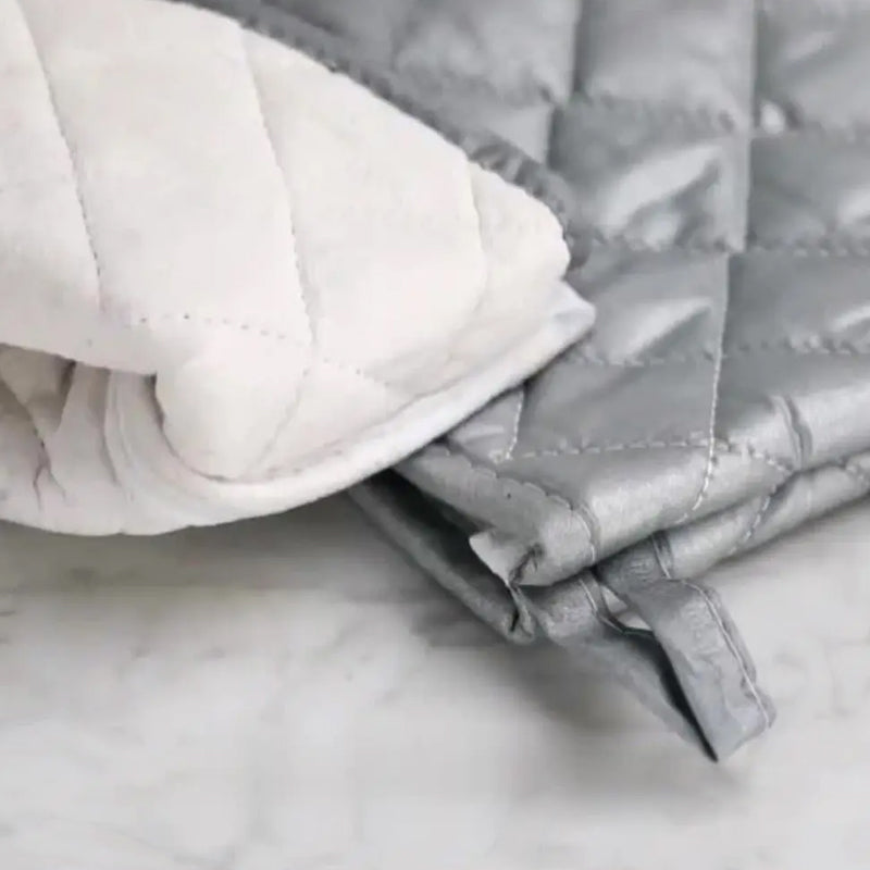 Close-up of a folded quilt with white and gray patterns on a marble surface