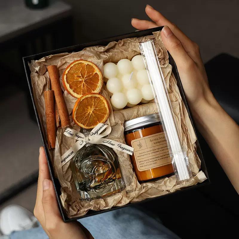 Gift box with candles, oranges, cinnamon, and a jar of honey held by hands.