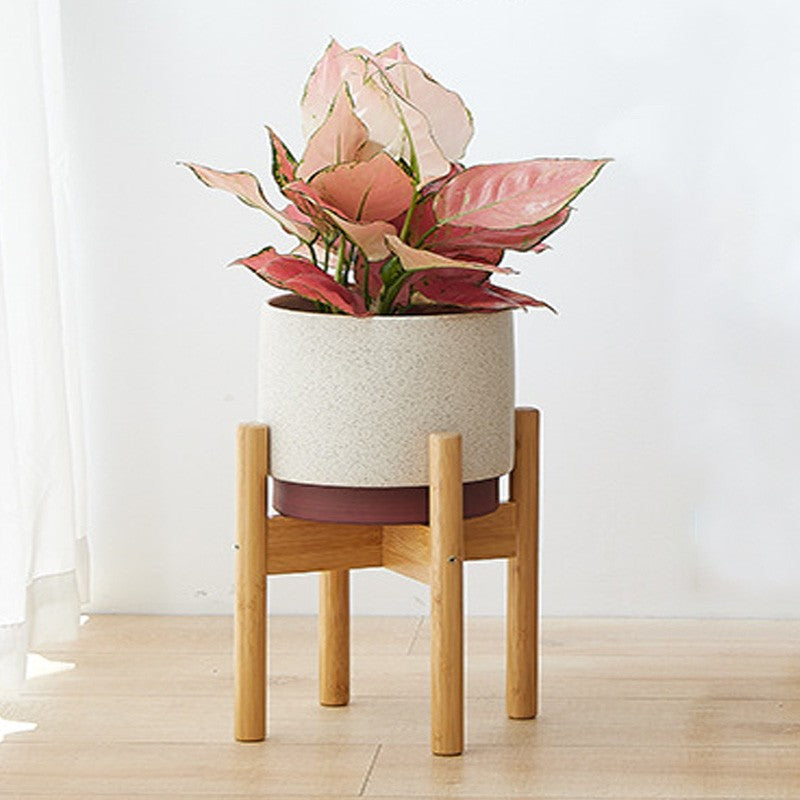 Floral arrangement in a textured pot on a wooden stand against a white wall.